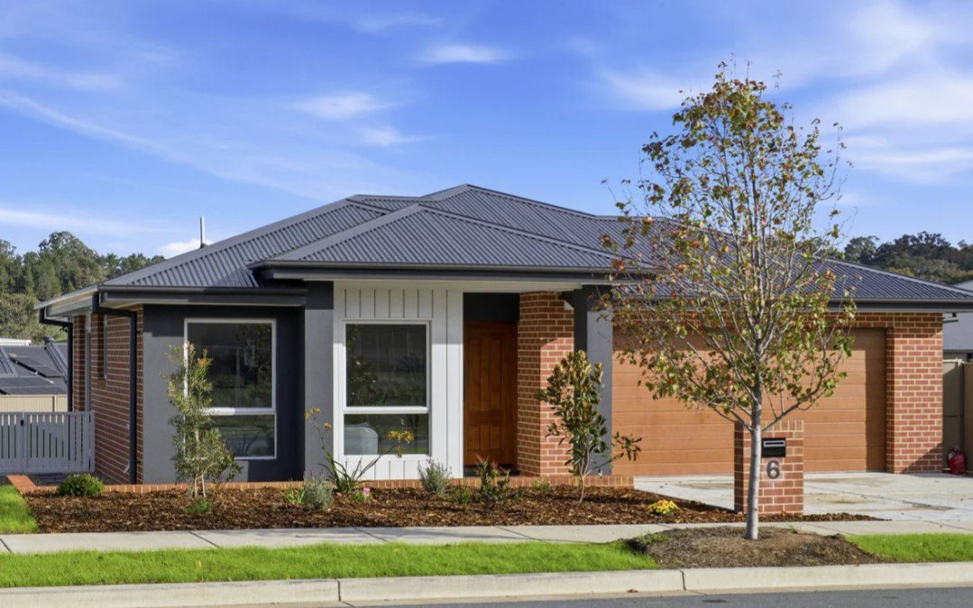 A completed single-storey home at Yarrah in red brick and dark render with a charcoal roof, a mulched front garden and a young ornamental tree at the kerb.