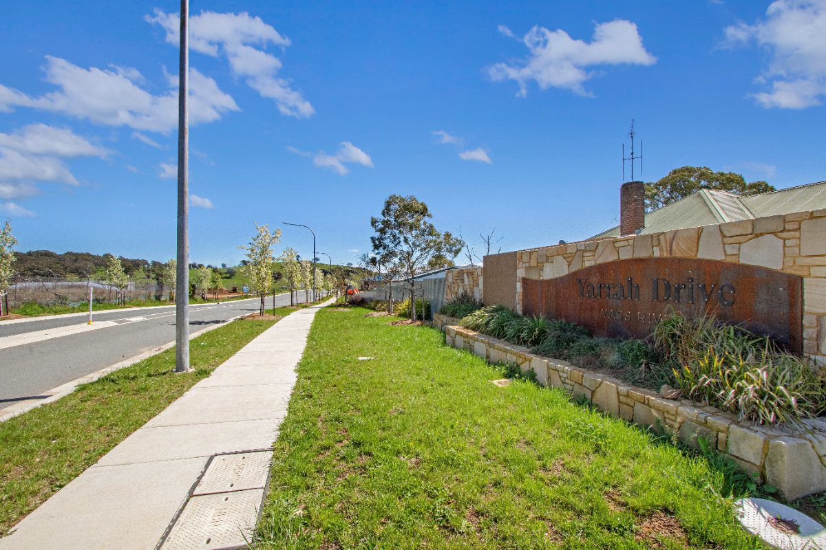 A footpath running beside a landscaped verge with grasses and shrubs in an established Yarrah street.