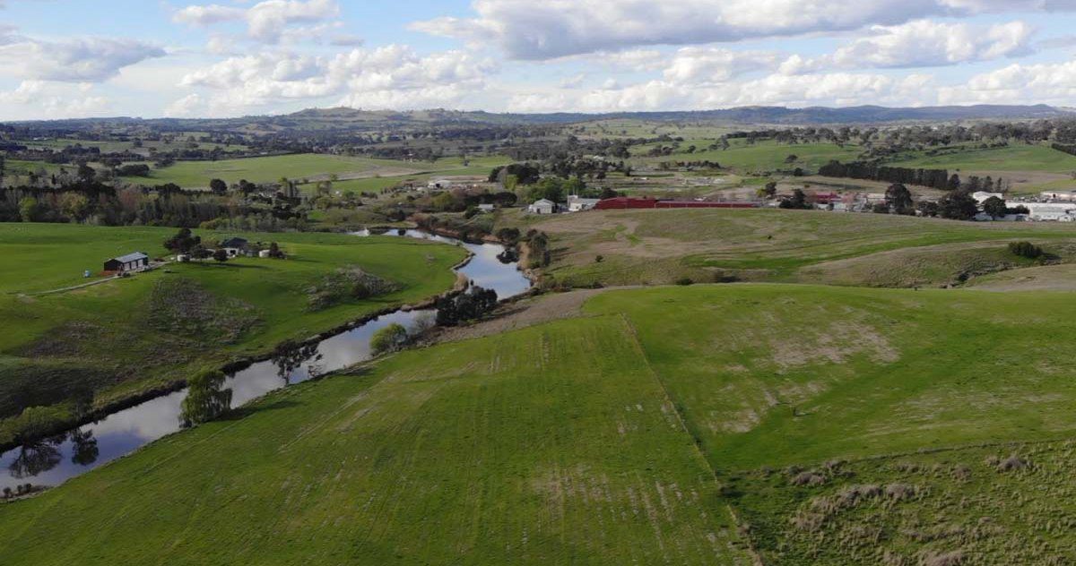 An aerial view of the Yass River winding between green paddocks, with the edge of Yass town and low hills on the horizon.