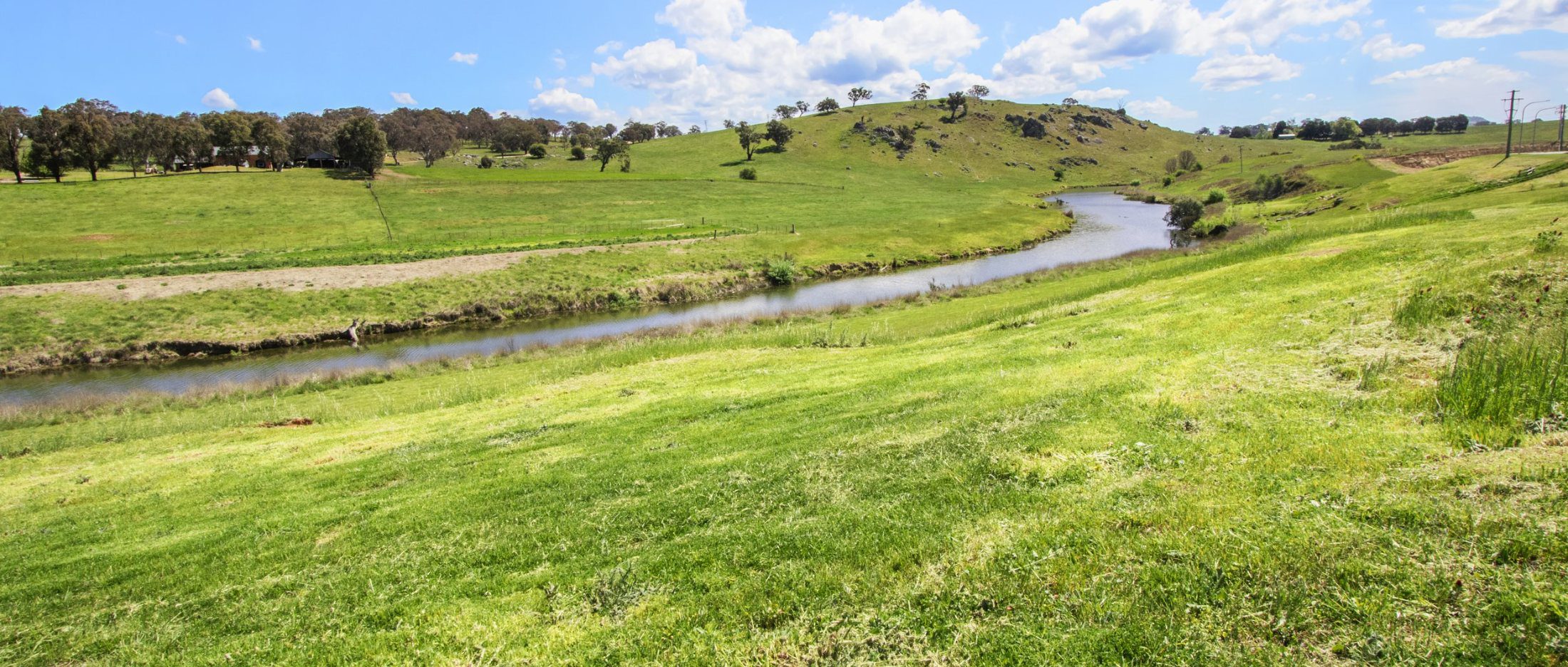 The Yass River curving through green pasture below low hills at Yarrah, with farm buildings on the far ridge.