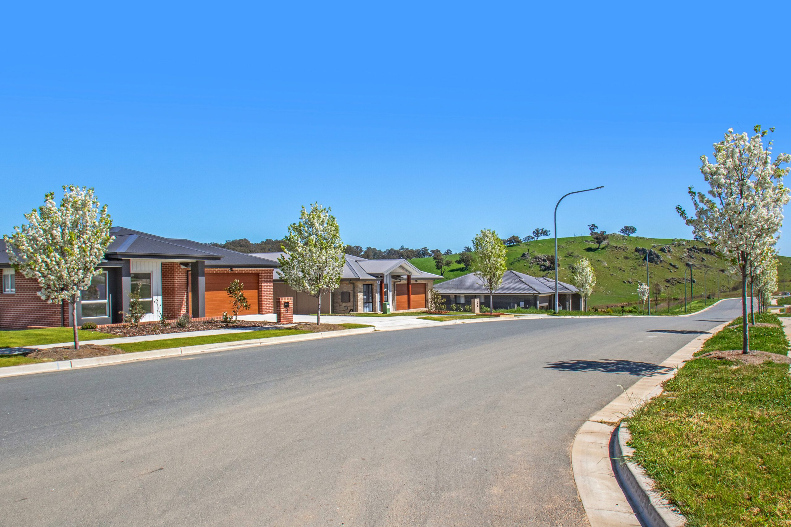 A completed two-storey home at Yarrah in white render with black-framed windows, a double garage, lawn and a gravel garden bed planted with grass trees.