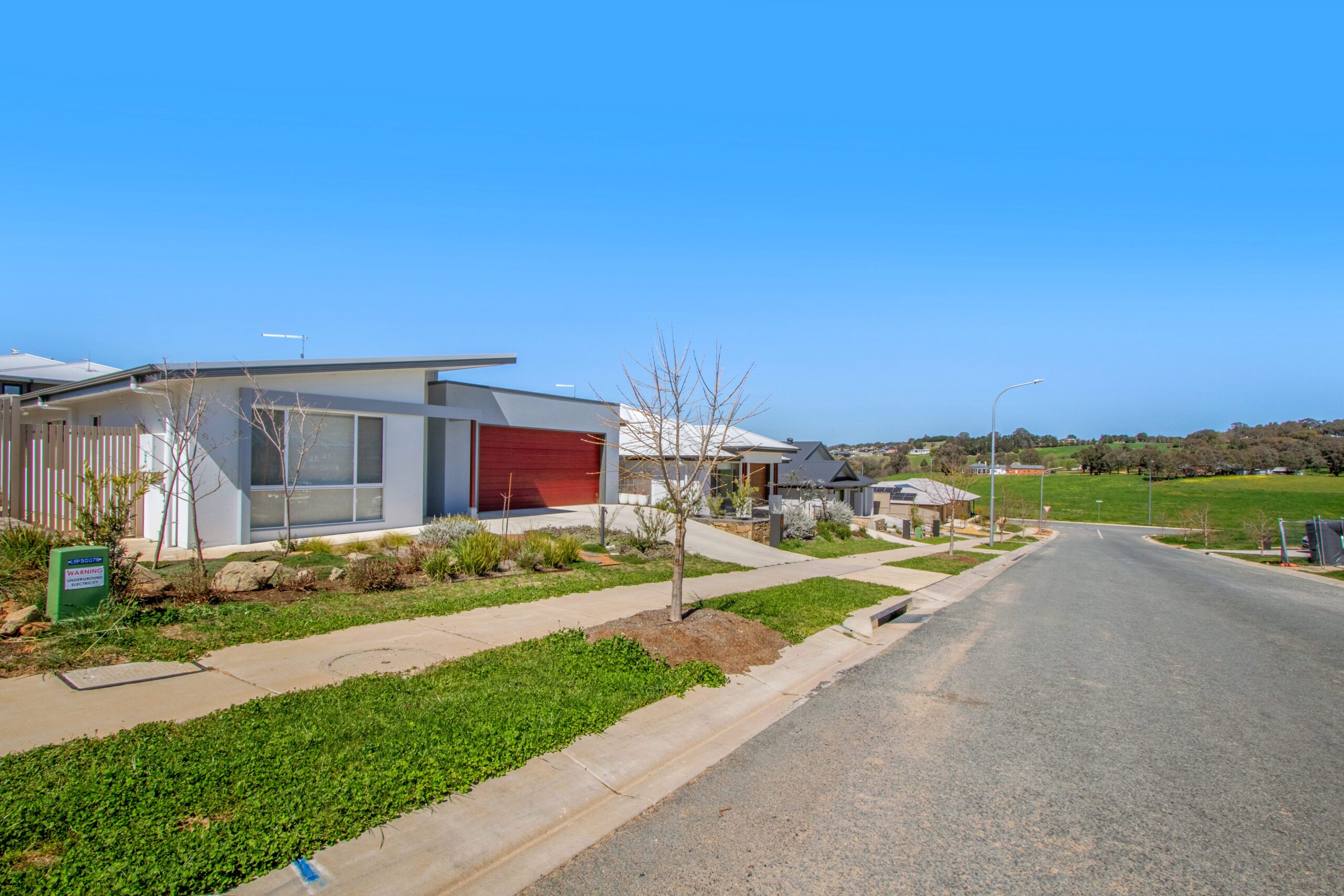 A completed two-storey home at Yarrah in white render with black-framed windows, a double garage, lawn and a gravel garden bed planted with grass trees.